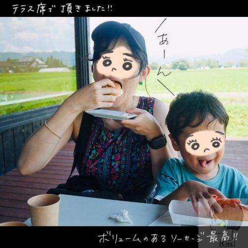 熊本　ヒバリカフェでランチ　女性と子供が田んぼと、山を望むテラス席で頂くホットドッグ