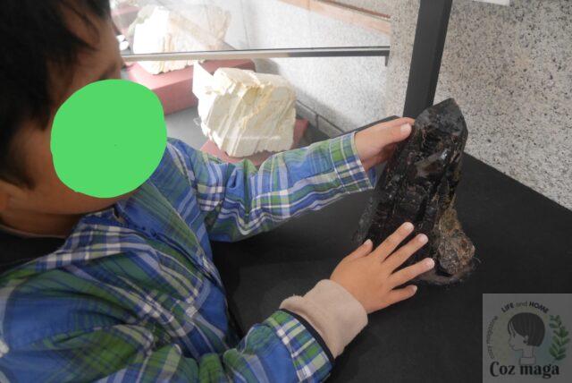 鉱物展示館（本館）の展示の１つである触れる黒曜石に小さな子どもが触っている
